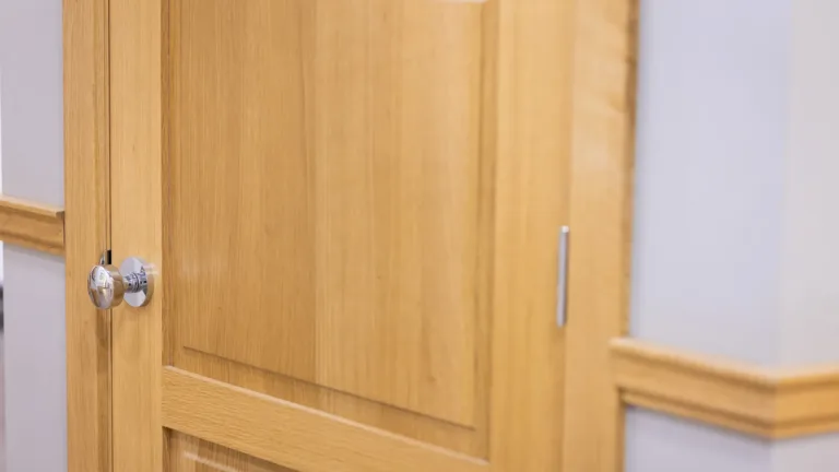 Close-up of a wooden door with a chrome and wood round door knob and light gray wall with wooden trim.