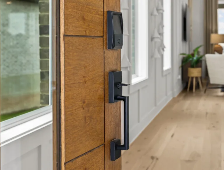 Close-up of a modern wooden door with a black electronic keypad lock and a black lever handle, opening into a bright room with wooden flooring and white paneled walls.