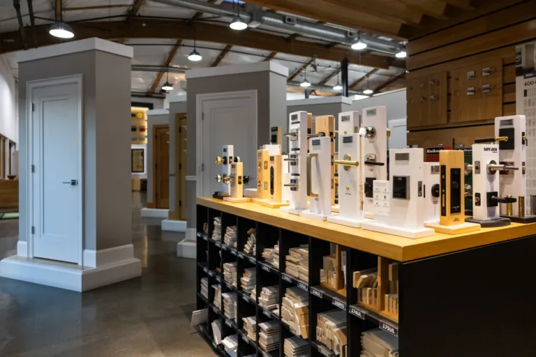 Interior of a hardware store showroom featuring white door displays and a long wooden counter displaying various lock and handle samples mounted on boards.