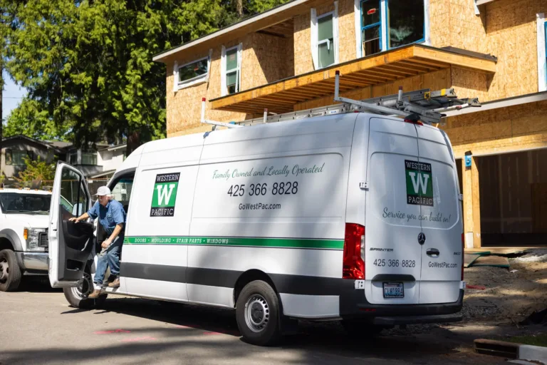 White Western Pacific service van parked in front of a wooden house under construction with a man stepping out of the driver's side door wearing a white cap and blue shirt.