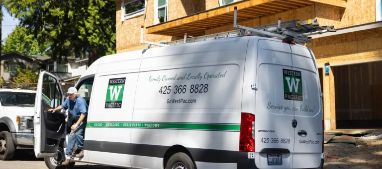 White Western Pacific service van parked in front of a wooden house under construction with a man stepping out of the driver's side door wearing a white cap and blue shirt.